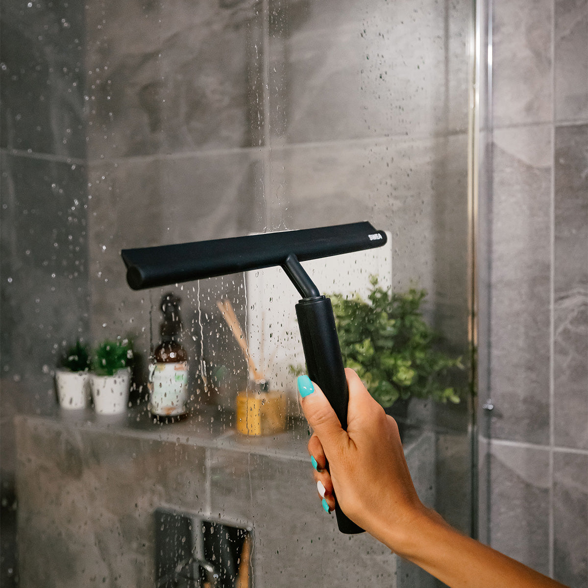 The SWEA black shower squeegee being demonstrated in a bathroom